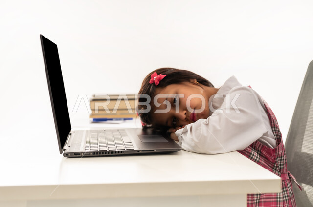 الشعور بالكسل والخمول، النوم على طاولة الدراسة، ايماءات النعاس والتعب والإرهاق، بورتريه مقرب لطالبة عربية خليجية سعودية ترتدي اليونيفورم المدرسي تقوم بإهمال دروسها، سلبيات التعلم عن بعد، تلميذة عمانية تقوم بهدر وضياع الوقت، خلفية بيضاء