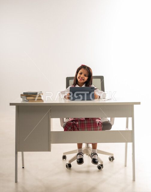 The concept of distance learning, the use of modern advanced technologies in scientific life, a portrait of an Arab Gulf Omani student wearing a school uniform and next to her virtual reality glasses, a Saudi student working on a tablet looking at the camera with expressions of pleasure, white background