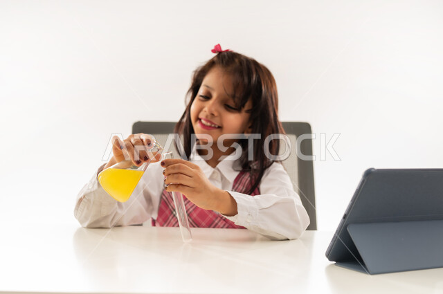 Using advanced modern technologies, choosing and determining the future profession from a young age, conducting experiments and biochemical reactions in the laboratory, close-up portrait of an Arab Gulf Omani girl wearing school uniform using test tubes, a Saudi student doing scientific research with expressions of pleasure, white background