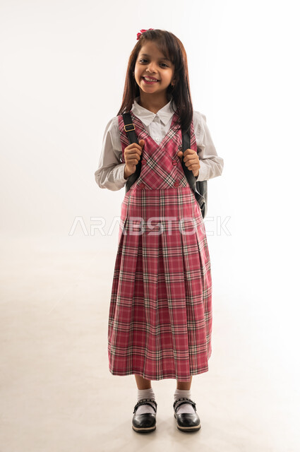 Preparing and getting ready for the start of the school year, an Omani student looking at the camera with gestures of happiness, the concept of the back-to-school season, a portrait of a Saudi Arabian Gulf student wearing a school uniform carrying a school bag, the desire to seek knowledge, the full-length body, white background