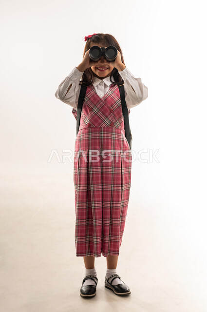 رؤية جديدة لتحسين جودة التعليم في دول الخليج العربي، بورتريه لتلميذة عربية خليجية سعودية ترتدي الزي المدرسي والحقيبة المدرسية تضع المنظار على عينيها لتقريب الاشياء البعيدة , طالبة عمانية تستعد للفصل الدراسي الجديد، صورة الجسم بالطول الكامل, خلفية بيضاء