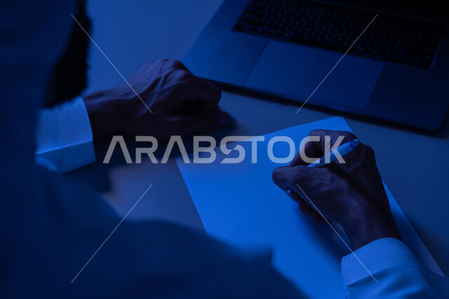 استخدام الاوراق البيضاء الفارغة في العمل، شاب سعودي يدون ويسجيل الملاحظات والمعلومات على الورق, إدارة الأعمال وتنظيمها، صورة مقربة ليدين شاب عربي خليجي اماراتي يرتدي الكندورة يقوم بكتابة المهام والأهداف اليومية