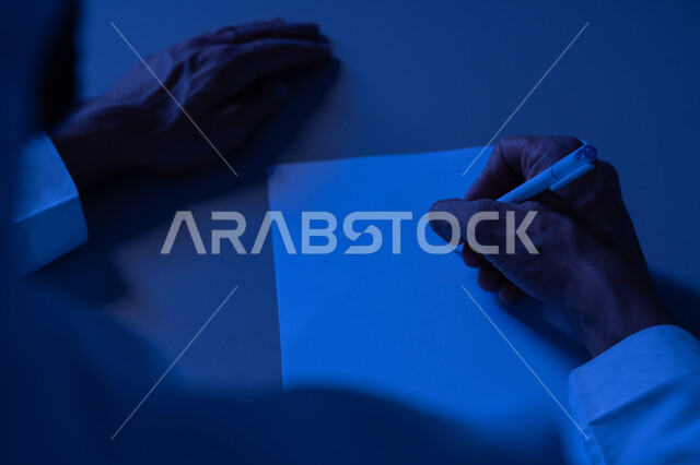 Business administration and organization, taking notes and recording information on paper, close-up of hands of young Arab Gulf Emirati man wearing traditional dress writing down daily tasks and goals