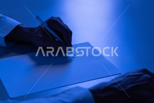 إدارة الأعمال وتنظيمها، استخدام الاوراق البيضاء الفارغة في العمل، شاب سعودي يدون ويسجيل الملاحظات والمعلومات على الورق, صورة مقربة ليدين شاب عربي خليجي اماراتي يرتدي الكندورة يقوم بكتابة المهام والأهداف اليومية