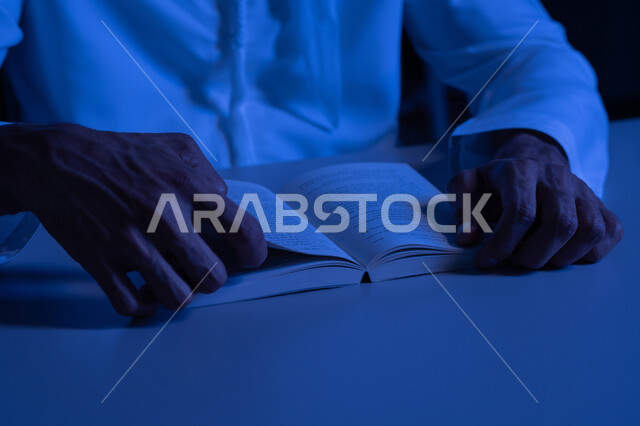 قضاء أوقات الفراغ بممارسة هواية المطالعة, مفهوم الثقافة والتعلم الذاتي, قراءة القصص والروايات الممتعة, صورة مقربة لأيدي رجل عربي خليجي إماراتي يرتدي الكندورة يمسك بيده الكتاب, تنمية الذخيرة الثقافية