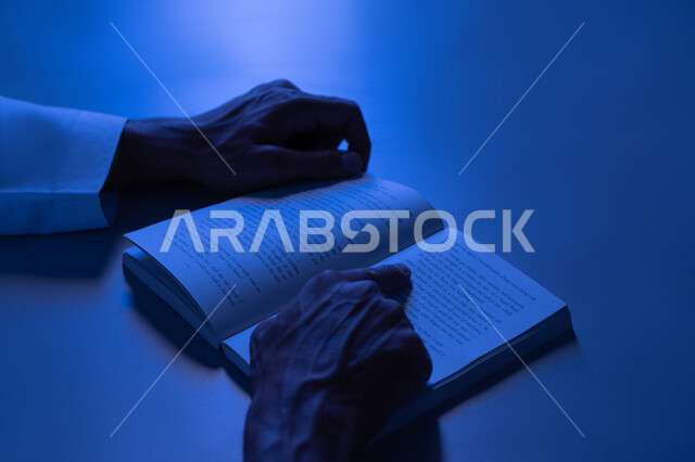 تنمية الذخيرة الثقافية، قضاء أوقات الفراغ بممارسة هواية المطالعة، مفهوم الثقافة والتعلم الذاتي, شاب سعودي يقوم بقراءة القصص والروايات الممتعة, صورة مقربة لأيدي رجل عربي خليجي إماراتي يرتدي الكندورة يقوم بتتبع الكتابة في الكتاب