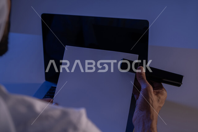 ترتيب وتنظيم البيانات، متابعة الخطط والمشاريع، قراءة الملاحظات والمعلومات، صورة مقربة لايدي رجل عربي خليجي اماراتي يحمل بيده الدباسة يقوم بجمع مجموعة من الاوراق الفارغة مع بعضها، شاب سعودي يدقق الوثائق الخاصة بالعمل