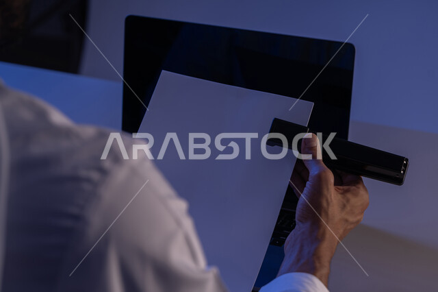 ترتيب وتنظيم البيانات، متابعة الخطط والمشاريع، قراءة الملاحظات والمعلومات، صورة مقربة لايدي رجل عربي خليجي اماراتي يحمل بيده الدباسة يقوم بجمع مجموعة من الاوراق الفارغة مع بعضها، شاب سعودي يدقق الوثائق الخاصة بالعمل