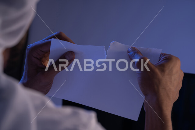 عدم الموافقة على شيء ما، صورة مقربة من الخلف لرجل عربي خليجي اماراتي يقوم بتمزيق ورقة بيضاء فارغة، شاب سعودي يعقد صفقة غير ناجحة، كسر القواعد المهنية في الشركات