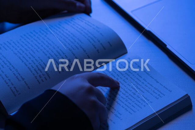 ممارسة هواية المطالعة، الاستمتاع بالأنشطة الترفيهية المفيدة في وقت الفراغ، مفهوم الثقافة والتعلم الذاتي, شابة سعودية تقوم بقراءة القصص والروايات الممتعة, صورة مقربة لأيدي امرأة عربية خليجية اماراتية ترتدي العباءة تقوم بتتبع السطور في الكتاب