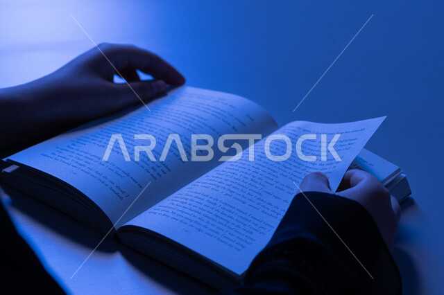 Enjoying useful recreational activities in free time, the concept of culture and self-learning, a young Saudi woman reading interesting stories and novels, a close-up of the hands of an Arab Gulf Emirati woman wearing an abaya practicing her hobby of reading