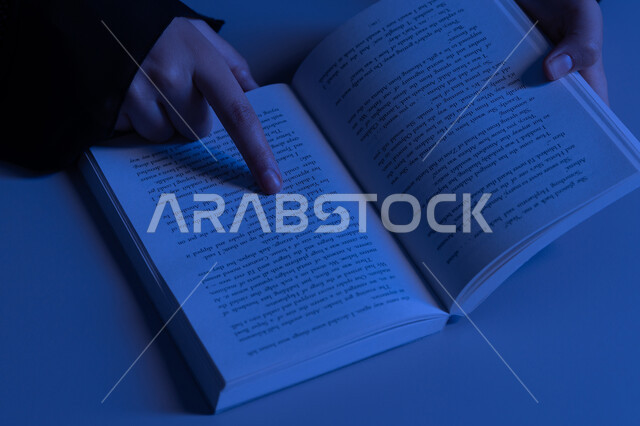 ممارسة هواية المطالعة، الاستمتاع بالأنشطة الترفيهية المفيدة في وقت الفراغ، مفهوم الثقافة والتعلم الذاتي, شابة سعودية تقوم بقراءة القصص والروايات الممتعة, صورة مقربة لأيدي امرأة عربية خليجية اماراتية ترتدي العباءة تقوم بتتبع السطور في الكتاب