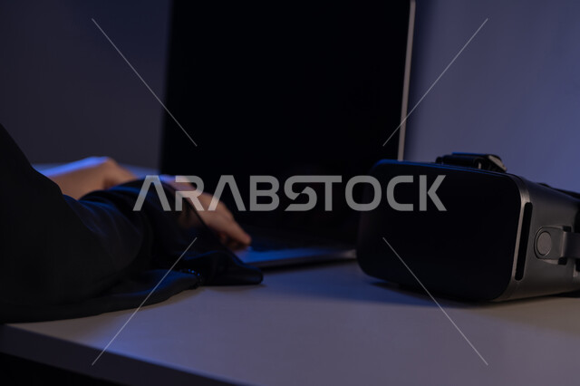 استخدام الأجهزة التكنولوجية والتقنيات الحديثة, محاكاة العالم الخيالي, صورة مقربة لايدي امرأة عربية خليجية اماراتية تقوم بإنجاز العمل على جهاز الحاسوب المحمول وبجانبها نظارة الفي ار, شابة سعودية تقوم بالنقرعلى لوحة المفاتيح