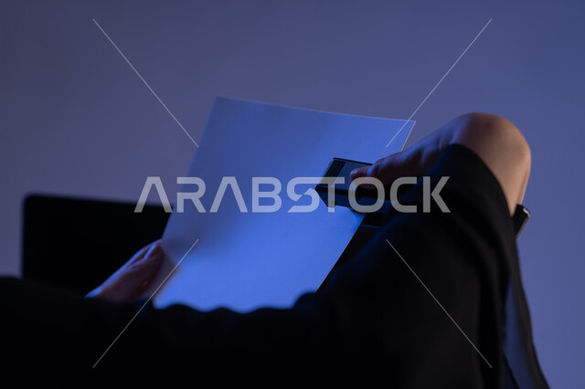 ترتيب وتنظيم البيانات، متابعة الخطط والمشاريع، قراءة الملاحظات والمعلومات، صورة مقربة من الجانب لايدي امرأة عربية خليجية اماراتية تحمل بيدها الدباسة تقوم بجمع مجموعة من الاوراق الفارغة مع بعضها، شابة سعودية تدقق الوثائق الخاصة بالعمل