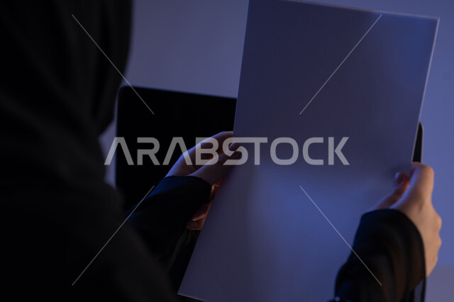 قراءة الملاحظات والمعلومات، متابعة الخطط والمشاريع، صورة مقربة من الجانب لامرأة عربية خليجية اماراتية تحمل بيدها مجموعة من الاوراق الفارغة، شابة سعودية تدقق الوثائق الخاصة بالعمل، ترتيب وتنظيم البيانات