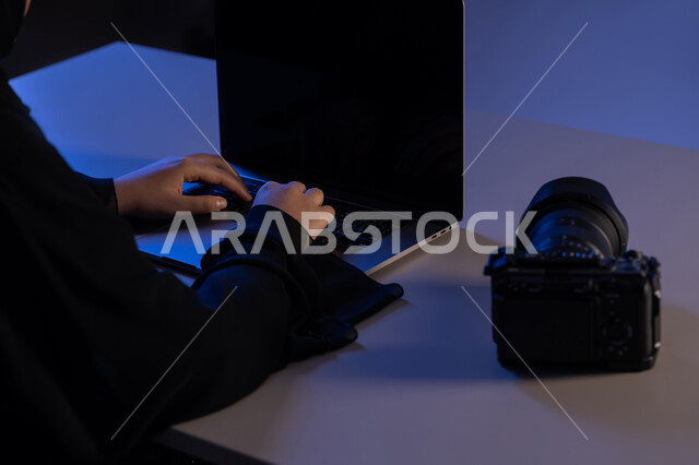 اتقان واحتراف مهنة التصوير، اداء مهام العمل بدقة واتقان، صورة مقربة من الجانب لايدي امرأة عربية خليجية اماراتية تعمل على جهاز الحاسوب المحمول بجانبها كاميرا فوتوغرافية، استخدام التقنيات الحديثة المتطورة، شابة سعودية تقوم بتعديل جلسة التصوير