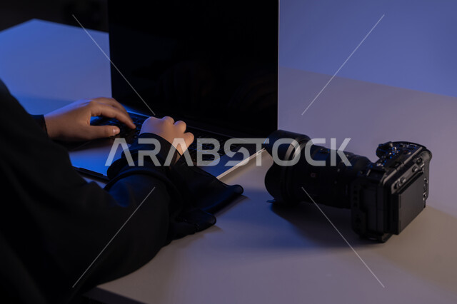 Performing work tasks with precision and mastery, mastery and professionalism in the photography profession, a close-up photo from the side of the hands of an Arab Gulf Emirati woman working on a laptop with a camera next to her, using modern advanced technologies, a young Saudi woman adjusting a photo session