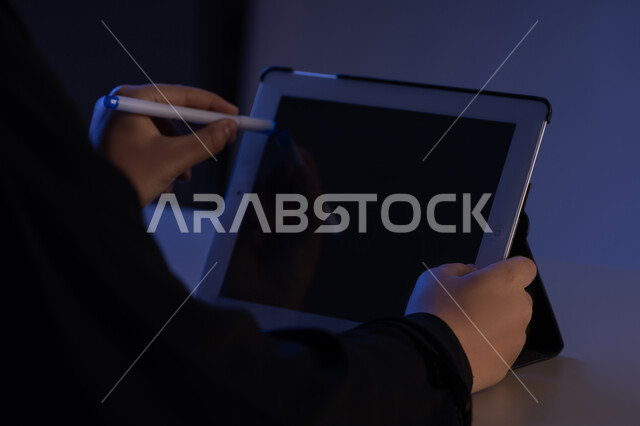 Using a tablet pen to take notes for work, following educational lessons, viewing a blank black screen, close-up of a Gulf Arab Emirati woman's hands completing tasks remotely, a young Saudi woman using an iPad, drawing pictures and electronic designs