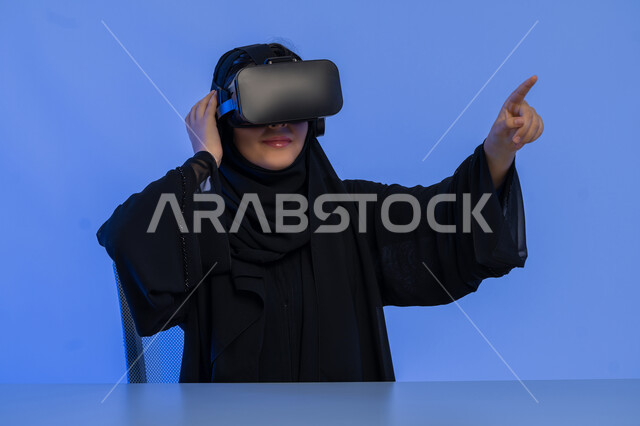 تحديد موقع شيء ما، محاكاة العالم الخيالي, استخدام الأجهزة التكنولوجية والتقنيات الحديثة, بورتريه مقرب لامرأة عربية خليجية اماراتية تشير باصبع السبابة لمكان ما، شابة سعودية ترتدي نظارة الواقع الافتراضي، خلفية زرقاء