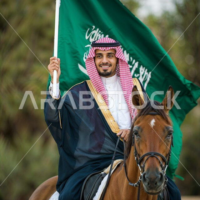 ذكرى يوم العلم 11 مارس, رجل عربي خليجي سعودي مبتسم يرتدي الثوب التقليدي والشماغ يمتطي حصان بني ويرفع بيده علم المملكة العربية السعودية, مفهوم الاعتزاز والفخر بالوطن, الاحتفال بالأعياد والمناسبات الوطنية, استذكار اليوم الوطني السعودي 23 سبتمبر