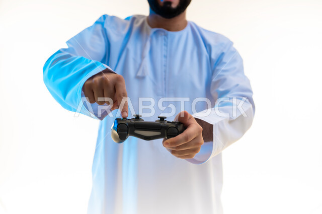 التفاعل والاندماج مع ألعاب الفيديو، قضاء وقت ممتع ومسلي، اجهزة وتقنيات الكترونية ترفيهيه حديثة, بورتريه مقرب لشاب عربي خليجي عماني يرتدي الدشداشة والكمة يقوم بالضغط على ازرار عصا التحكم بايماءات الدهشة، خلفية بيضاء