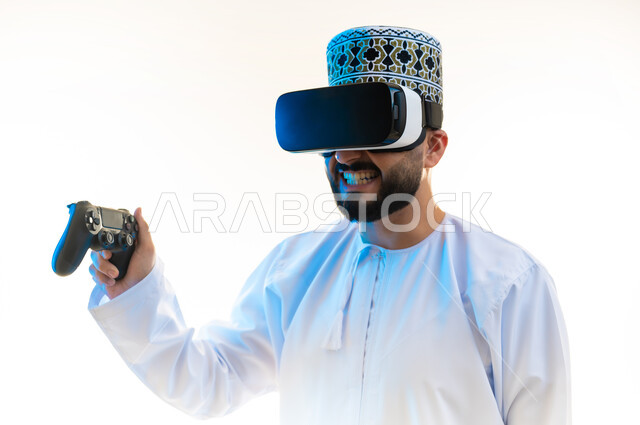 Merging the fantasy world with fun and entertainment, using technological devices and modern techniques, close-up portrait of an Arab Gulf Omani man wearing a dishdasha, a kimono and virtual reality glasses, holding a joystick in his hand, playing entertaining video games with gestures of enjoyment and enthusiasm, white background