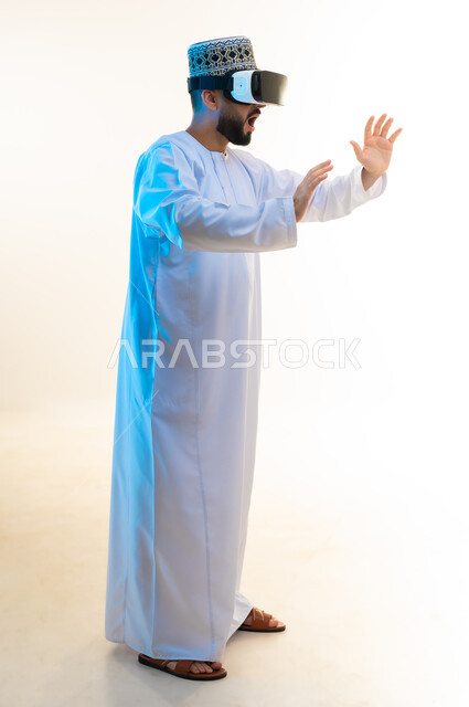 محاولة تجنب شيء ما، محاكاة العالم الخيالي, بورتريه من الجانب لرجل عربي خليجي عماني يرتدي الدشداشة والكمة يضع نظارة ثلاثية الأبعاد يتفاعل معها، رفع اليدين بإيماءات الصدمة والاندهاش، مشاهدة الأفلام باستخدام تقنيات الواقع الافتراضي, الجسم بالطول الكامل، خلفية بيضاء