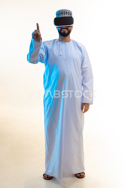 الاندماج ومحاكاة العالم الخيالي, مشاهدة الأفلام عبر تقنيات الواقع الافتراضي, إيماءات النقر على عنصر ما، بورتريه لرجل عربي خليجي عماني يرتدي الدشداشة والكمة يضع نظارة ثلاثية الأبعاد يرفع إصبع السبابة للأعلى، الجسم بالطول الكامل، خلفية بيضاء