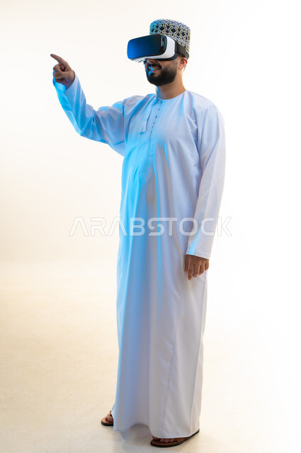 إيماءات النقر على عنصر ما، بورتريه لرجل عربي خليجي عماني يرتدي الدشداشة والكمة يضع نظارة ثلاثية الأبعاد يرفع إصبع السبابة للأعلى، الاندماج ومحاكاة العالم الخيالي, مشاهدة الأفلام عبر تقنيات الواقع الافتراضي, الجسم بالطول الكامل، خلفية بيضاء