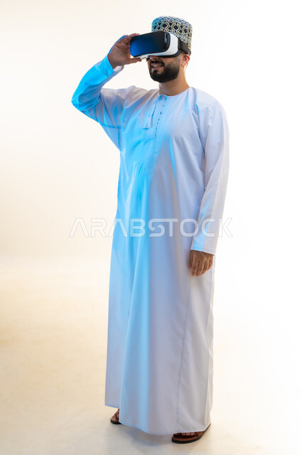 قضاء أوقات ممتعة بمشاهدة الأفلام باستخدام تقنيات الواقع الافتراضي, التطور التقني والتكنولوجي, الاندماج ومحاكاة العالم الخيالي, بورتريه لرجل عربي خليجي عماني يرتدي الدشداشة والكمة ونظارة ثلاثية الأبعاد، الجسم بالطول الكامل، خلفية بيضاء