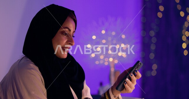 An Arab woman doing a photo session at home, using a mobile phone, remote work, e-marketing, surfing the Internet, the concept of using technology and modern technology devices, entertainment and entertainment, using social media, the concept of addiction