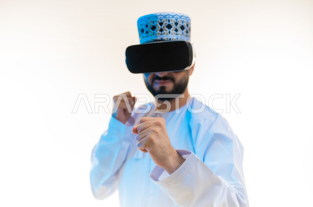 Training combat moves through video games, practicing self-defense with technological techniques, close-up portrait of an Arab Gulf Omani man wearing a dishdasha, a kummah and virtual reality glasses raising his hands with boxing and wrestling gestures, releasing negative energy, white background
