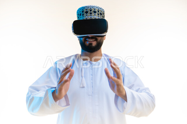 مشاهدة الأفلام باستخدام تقنيات الواقع الافتراضي, الاندماج ومحاكاة العالم الخيالي, بورتريه مقرب لرجل عربي خليجي عماني يرتدي الدشداشة والكمة يضع نظارة ثلاثية الأبعاد يرفع يديه لإمساك عنصر معين، محاولة تحديد حجم شيء ما، خلفية بيضاء