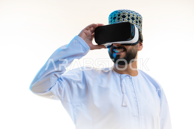 Technical and technological development, integration and simulation of the imaginary world, close-up portrait of an Arab Gulf Omani man wearing a dishdasha, a turban and 3D glasses with his hand on them, having fun watching movies using virtual reality technologies, white background