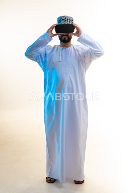قضاء أوقات ممتعة بمشاهدة الأفلام باستخدام تقنيات الواقع الافتراضي, الاندماج ومحاكاة العالم الخيالي, بورتريه لرجل عربي خليجي عماني يرتدي الدشداشة والكمة ونظارة ثلاثية الأبعاد يضع يديه عليها، التطور التقني والتكنولوجي, الجسم بالطول الكامل، خلفية بيضاء