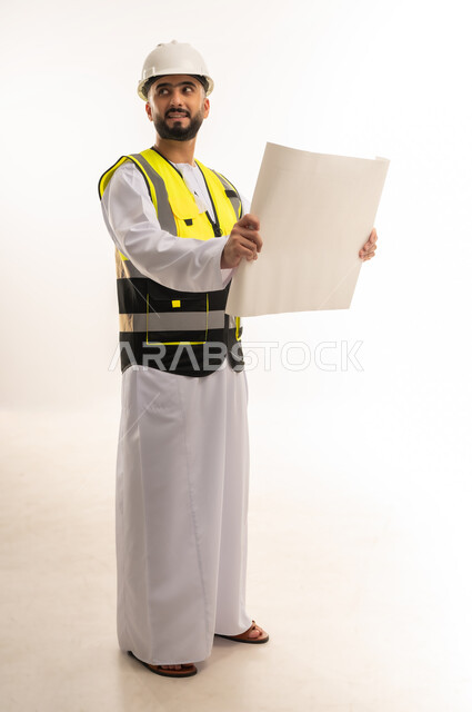 Supervising construction engineering projects, reviewing project plans, portrait of an Arab Gulf Omani engineer wearing a dishdasha, helmet and protective vest holding an engineering plan looking at something, youth professions and jobs, full body image, white background