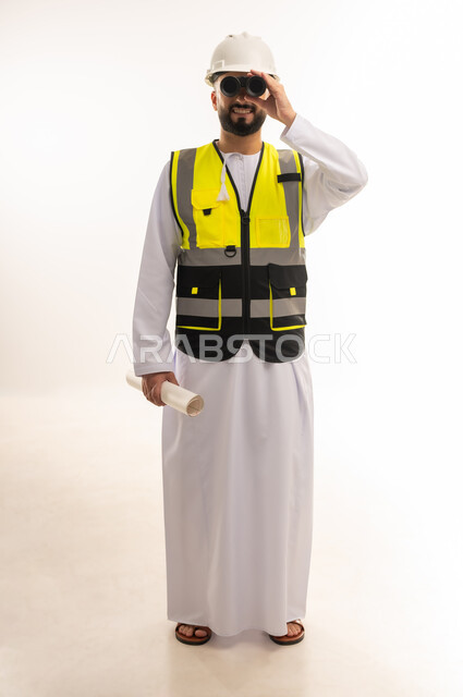 Following the progress of construction engineering projects, seeing distant objects, portrait of an Arab Gulf Omani engineer wearing a dishdasha, helmet and protective vest looking through binoculars at something holding a plan in his hand, youth professions and jobs, full-length body image, white background