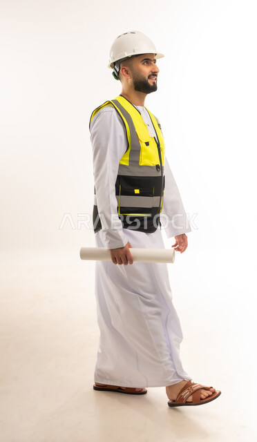 Walking to a specific place to complete work, concept of architectural construction and engineering, portrait of an Arab Gulf Omani engineer wearing a dishdasha, helmet and protective vest holding a plan in his hand, following up on the progress of construction projects, youth professions and jobs, full-length body image, white background