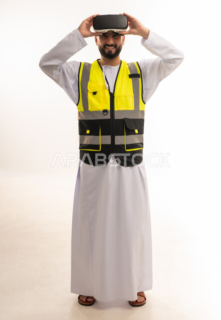 دمج التكنولوجيا بالمجالات الهندسية، تطور المجال الهندسي، التفاعل مع الهندسة الافتراضية، بورتريه لمهندس عربي خليجي عماني يرتدي الدشداشة والسترة الخاصة بالعمل يضع نظارة الواقع الافتراضي على رأسه ينظر إلى الكاميرا بإيماءات السرور، رؤية مستقبلية 2030، خلفية بيضاء