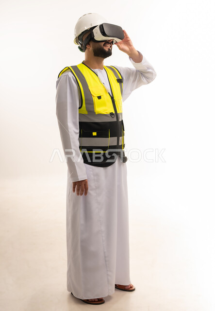 تجسيد ومشاهدة المشاريع الهندسية بالاعتماد على التكنولوجيا، استخدام التقنيات الحديثة والمتطورة في مجال التصاميم المعمارية، بورتريه لمهندس عربي خليجي عماني يرتدي الدشداشة والسترة وخوذة الحماية يلبس نظارات الفي آر ثلاثية الأبعاد، الجسم بالطول الكامل، خلفية بيضاء