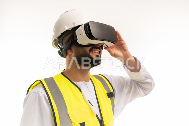 محاكاة العالم الافتراضي، مشاهدة المشاريع الهندسية بالاعتماد على التكنولوجيا، استخدام التقنيات الحديثة والمتطورة في مجال التصاميم المعمارية، بورتريه مقرب لمهندس عربي خليجي عماني يرتدي الدشداشة والسترة وخوذة الحماية يلبس نظارات في آر ثلاثية الأبعاد، خلفية بيضاء