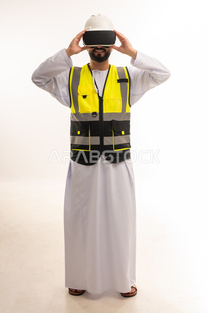 Using modern and advanced technologies in the field of architectural designs, relying on technology to embody and view engineering projects, portrait of an Arab Gulf Omani engineer wearing a dishdasha, jacket and protective helmet, wearing 3D VR glasses, full-length body, white background