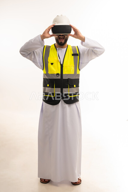 الاعتماد على التكنولوجيا لتجسيد ومشاهدة المشاريع الهندسية، استخدام التقنيات الحديثة والمتطورة في مجال التصاميم المعمارية، بورتريه لمهندس عربي خليجي عماني يرتدي الدشداشة والسترة وخوذة الحماية يلبس نظارات الفي آر ثلاثية الأبعاد، الجسم بالطول الكامل، خلفية بيضاء