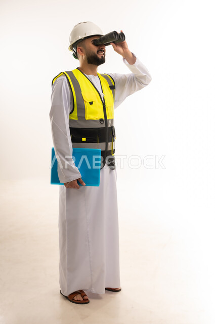 استخدام المنظار ثنائي العينين في مشاهدة الأشياء البعيدة، مفهوم الإشراف على المشاريع الإنشائية، إدارة الأعمال والاطلاع على آخر المستجدات، بورتريه لمهندس عربي خليجي عماني يرتدي الدشداشة والسترة وخوذة الحماية يمسك بيده ملف أزرق، الجسم بالطول الكامل، خلفية بيضاء