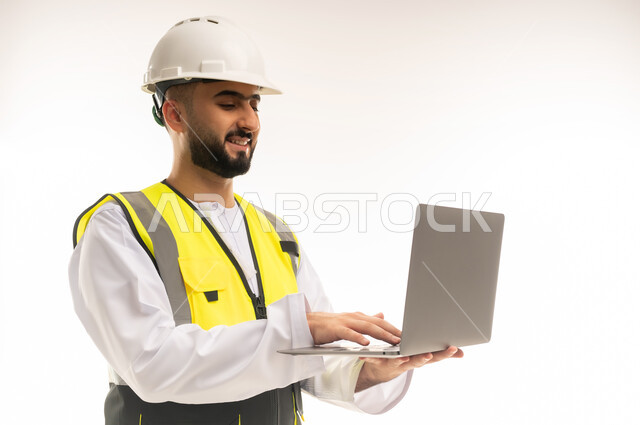 اعتماد القطاع الهندسي على التقنيات الحديثة والتكنولوجيا لتسيير الأعمال، استخدام التكنولوجيا المتطورة في الإشراف على العمل، بورتريه مقرب لمهندس عربي خليجي عماني يرتدي الدشداشة والسترة وخوذة الحماية يمسك الحاسوب المحمول ويقوم بمتابعة أعماله عن بعد، خلفية بيضاء