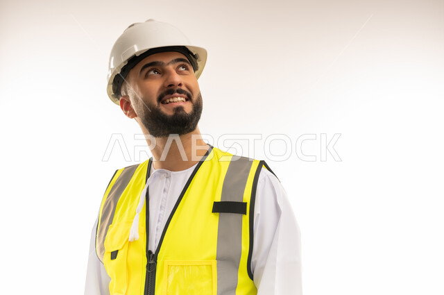 التطلع إلى الستقبل المشرق، مهن ووظائف للشباب في السلطنة، العمل في المجالات الهندسية المعمارية، الأحلام والرؤى المستقبلية، بورتريه مقرب لمهندس عربي خليجي عماني يرتدي الدشداشه والسترة وخوذة الحماية ينظر إلى مكان ما بإيماءات الاندماج والبشاشة، خلفية بيضاء