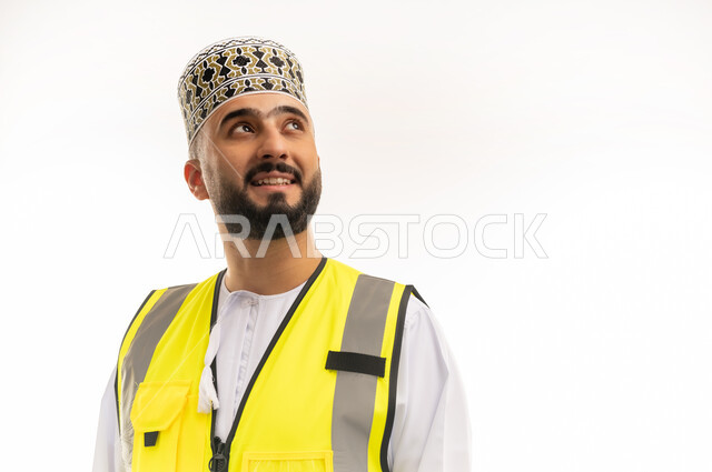 Careers and jobs for young people in the Sultanate of Oman, concept of engineering and architectural construction, work in the engineering sector, close-up portrait of an Arab Gulf Omani engineer wearing a dishdasha, a sleeve and a protective vest looking at a place with gestures of integration and concentration, white background
