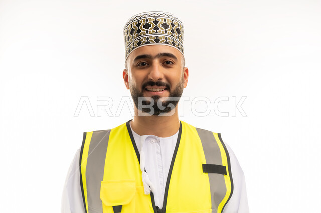 Concept of engineering and architectural construction, working in the engineering sector, close-up portrait of an Arab Gulf Omani engineer wearing a dishdasha, a sleeve and a protective vest, looking at the camera with gestures of pleasure and happiness, professions and jobs for young people in the Sultanate of Oman, white background