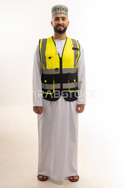 Working in the engineering sector, the concept of engineering and architectural construction, a portrait of an Arab Gulf Omani engineer wearing a dishdasha, a sleeve and a protective vest, standing straight and looking at the camera with gestures of pleasure and happiness, professions and jobs for young people in the Sultanate of Oman, full-length body, white background