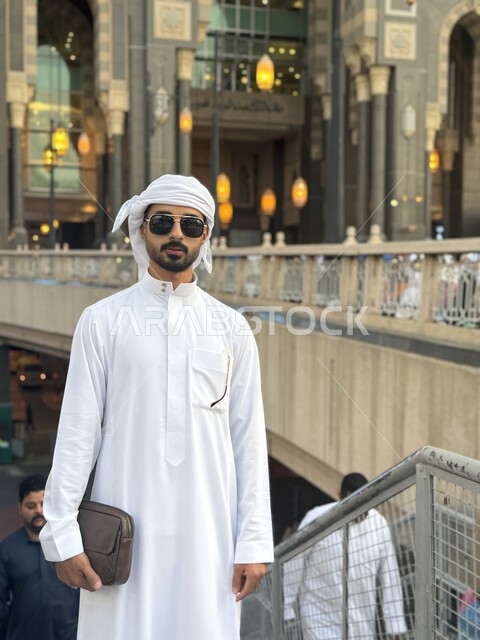  التعرف على المعالم والأماكن المشهورة في المملكة العربية السعودية، سائح عربي خليجي إماراتي يرتدي الثوب التقليدي والعمامة والنظارة الشمسية يتجول في الأسواق التجارية لمدينة مكة المكرمة، شاب زائر لبيت الله الحرام لأداء مناسك الحج والعمرة، مفهوم السياحة والسفر